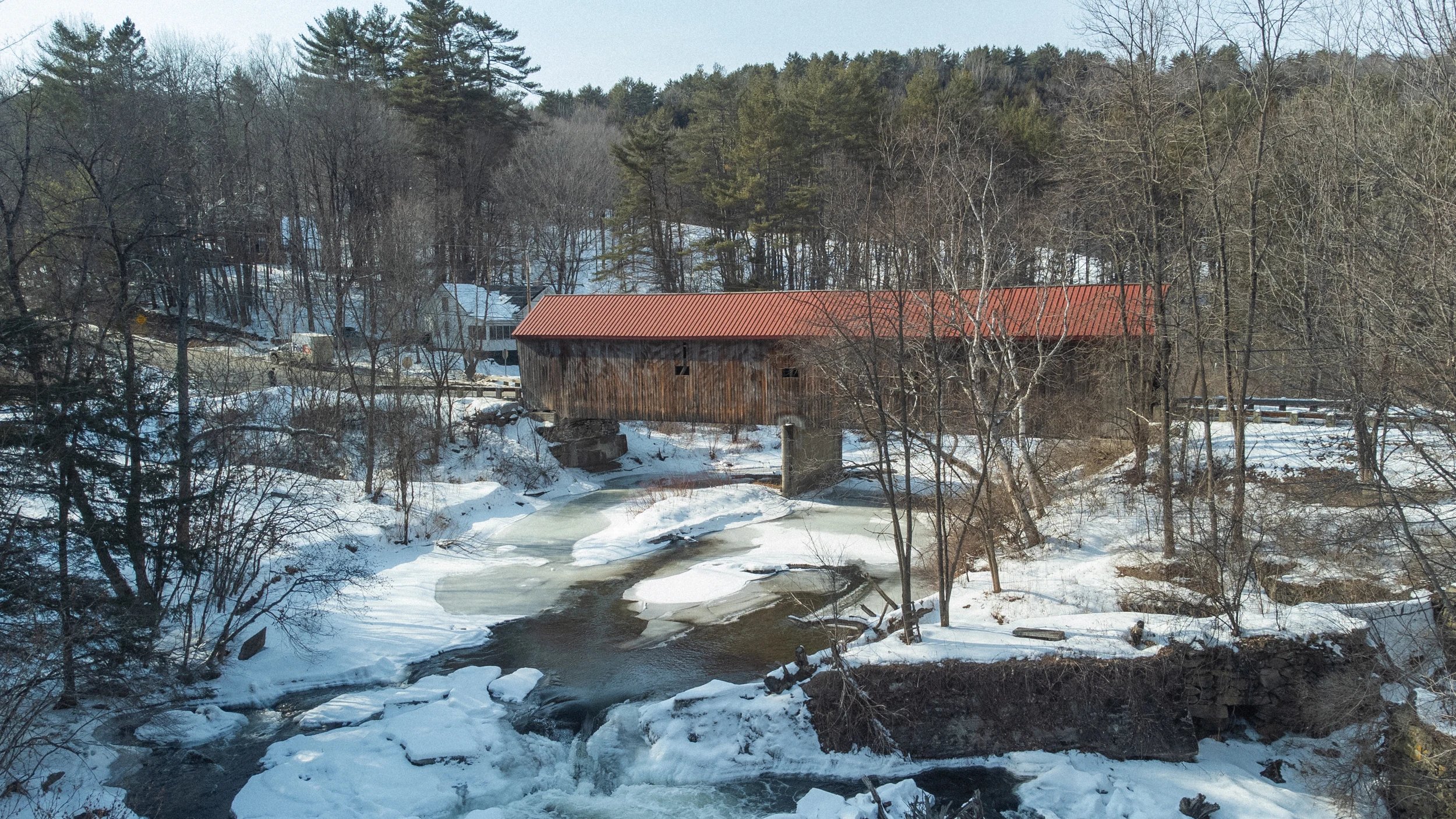 A red-roofed covered bridge framed by winter trees